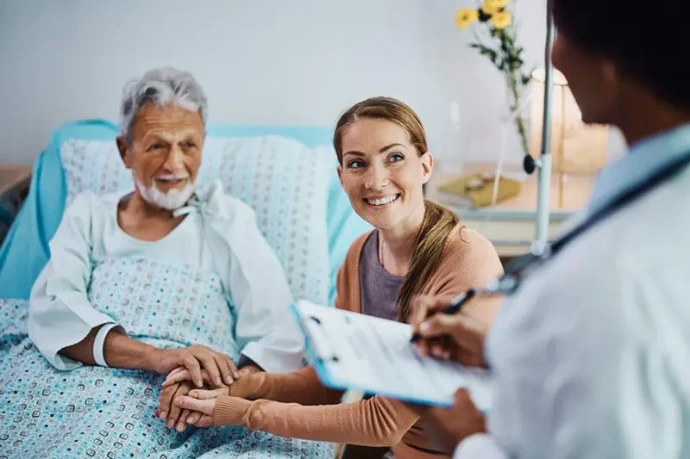 A doctor at the bedside while a family caregiver listens